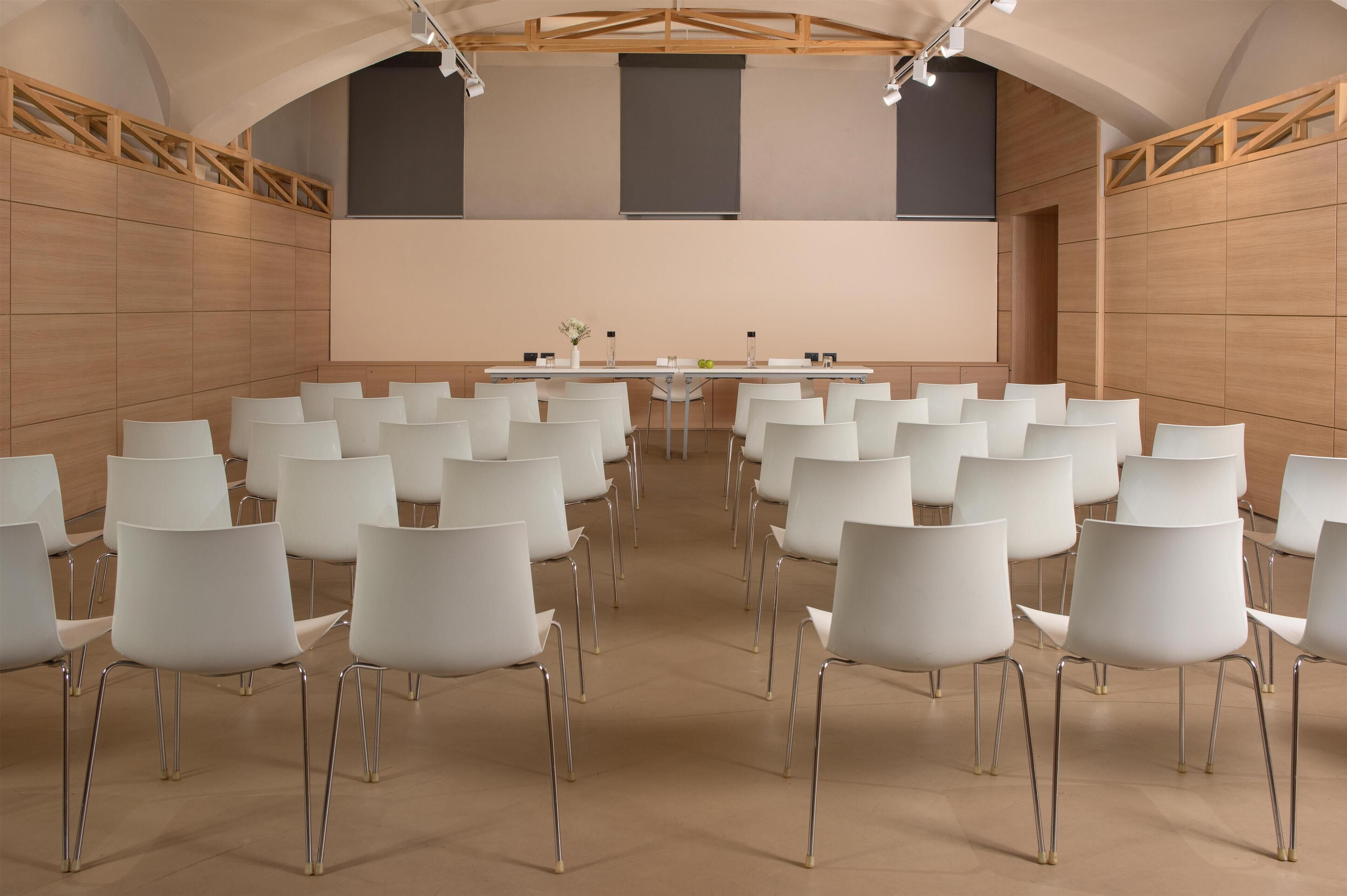 Una sala conferenze con un lungo tavolo, sedie bianche e pareti rivestite in legno.