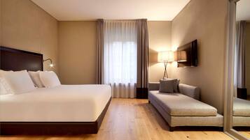 A hotel room with a large bed, a sofa, a TV, and a mirror.