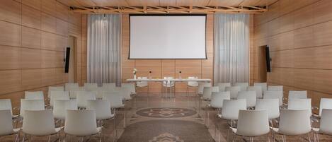 A conference room with a large screen, white chairs, and a long table.