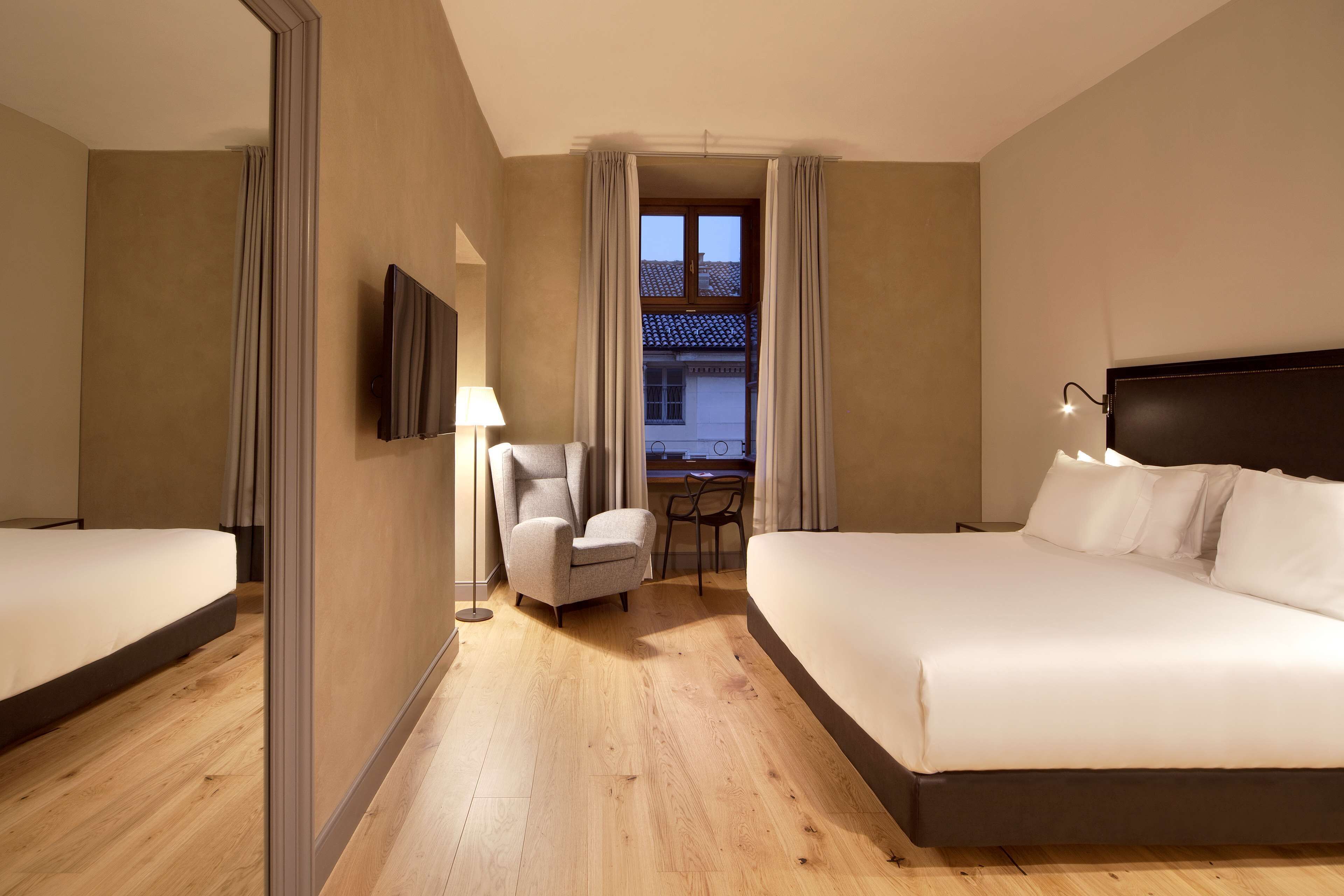 A hotel room with two beds, a desk, a chair, a TV, and a window with curtains.