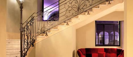 A staircase with ornate metal railings, a red velvet sofa, and a television mounted on the wall.