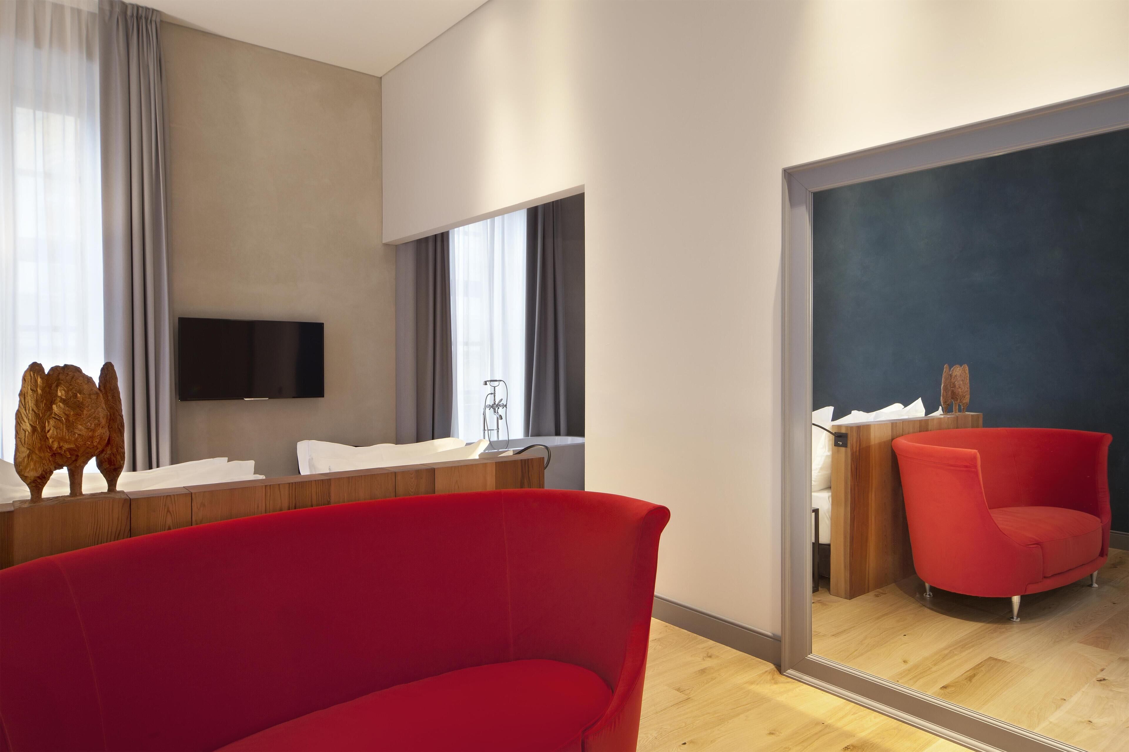 Una habitación de hotel moderna con un espejo grande, un sofá rojo, un tocador de madera y un televisor de pantalla plana montado en la pared.