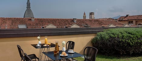 Una terraza con una mesa dispuesta para dos personas, que incluye una botella de jugo, un plato de comida y un florero con flores.