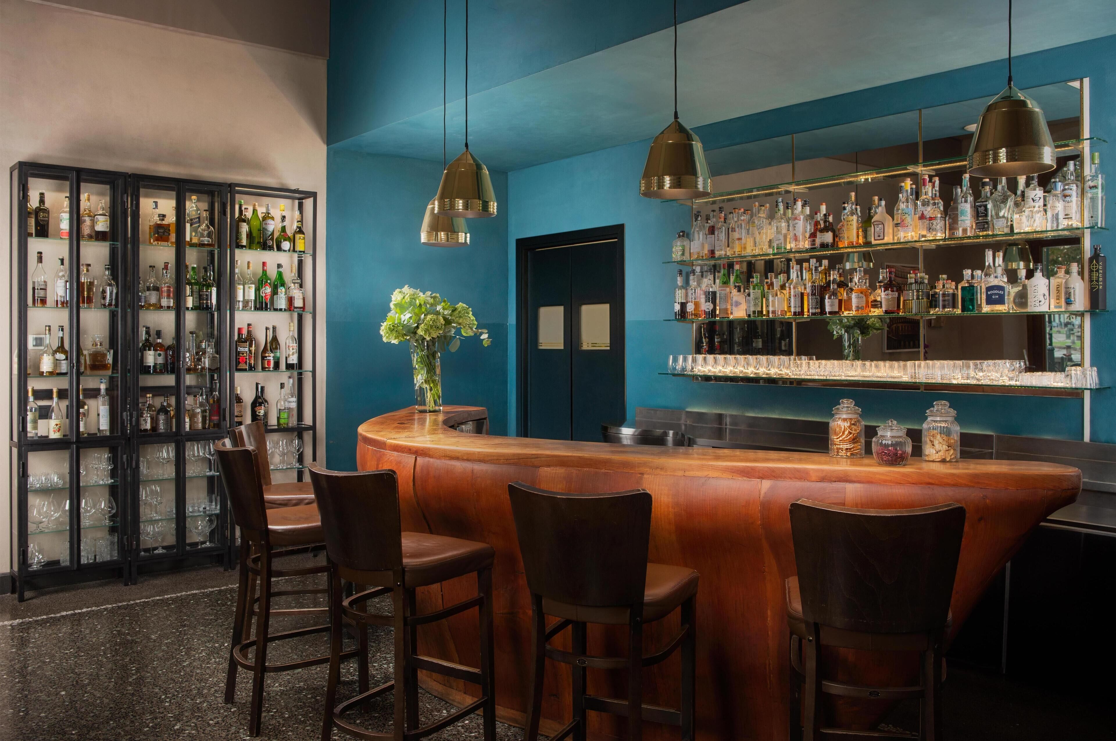 A bar area with a wooden counter, bar stools, and shelves stocked with liquor bottles.