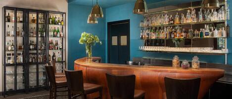 A bar area with a wooden counter, bar stools, and shelves stocked with liquor bottles.