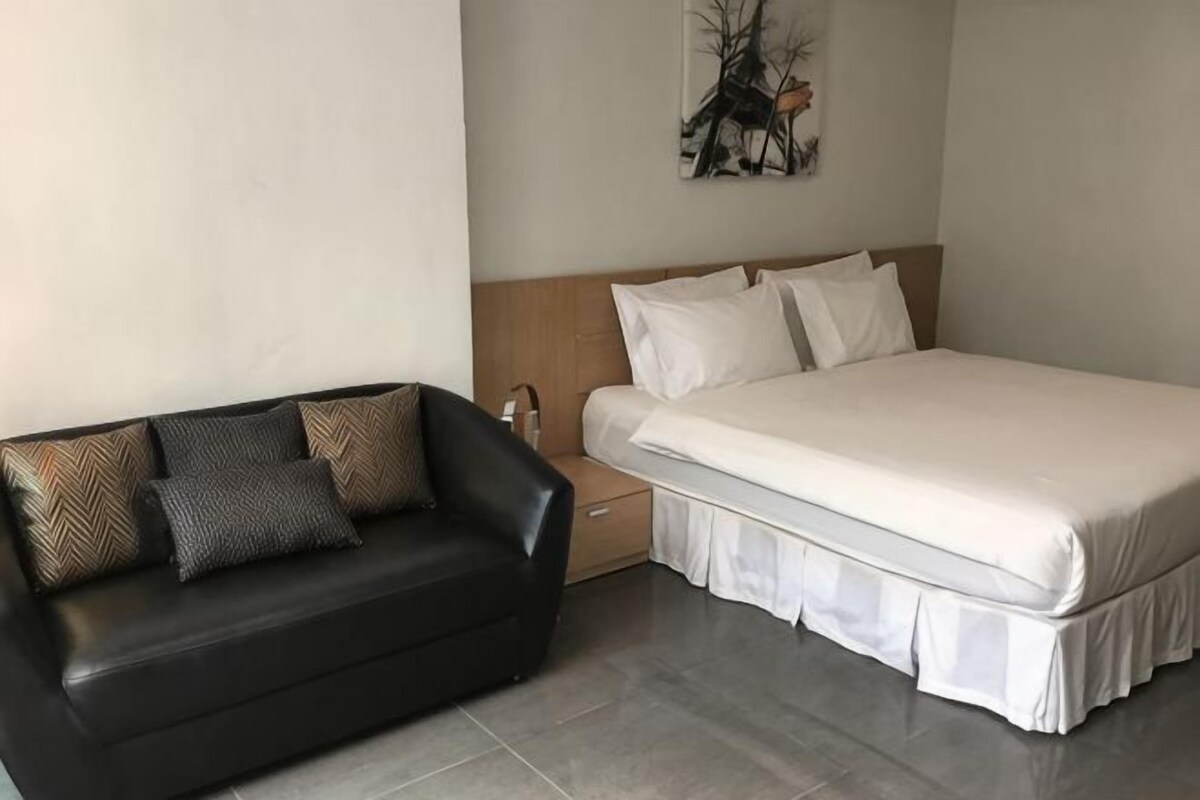 Una habitación de hotel con una cama, un sofá de cuero negro, una mesita de noche y una obra de arte colgada en la pared.
