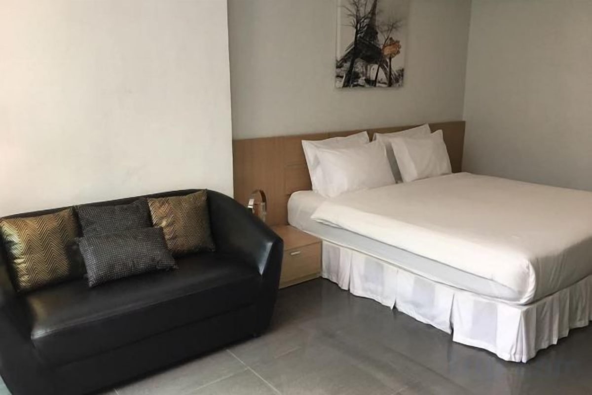 Une chambre à coucher comprenant un lit, une table de chevet, un canapé en cuir noir et une œuvre d’art accrochée au mur.
