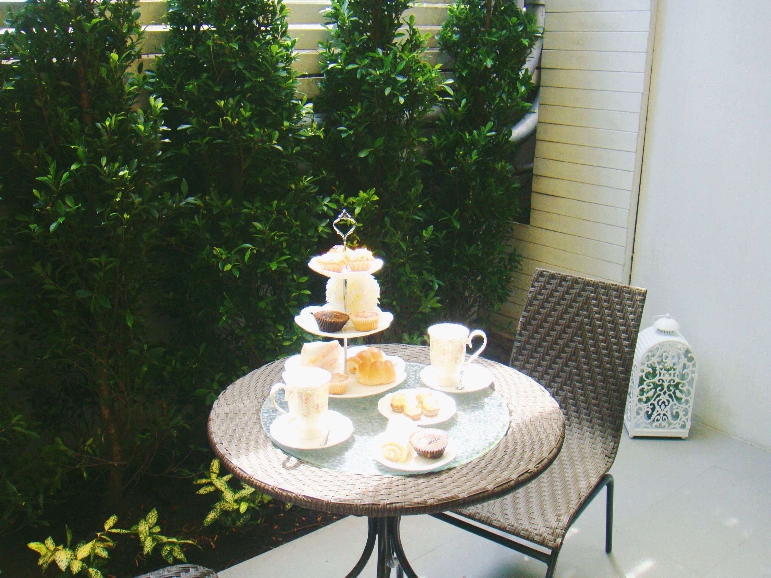 A round wicker table with a tiered dessert stand, a wicker chair, and a white lantern.