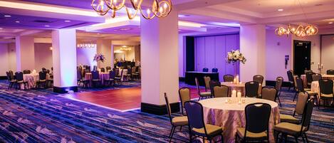 A spacious banquet hall with round tables, chairs, and a carpeted floor.