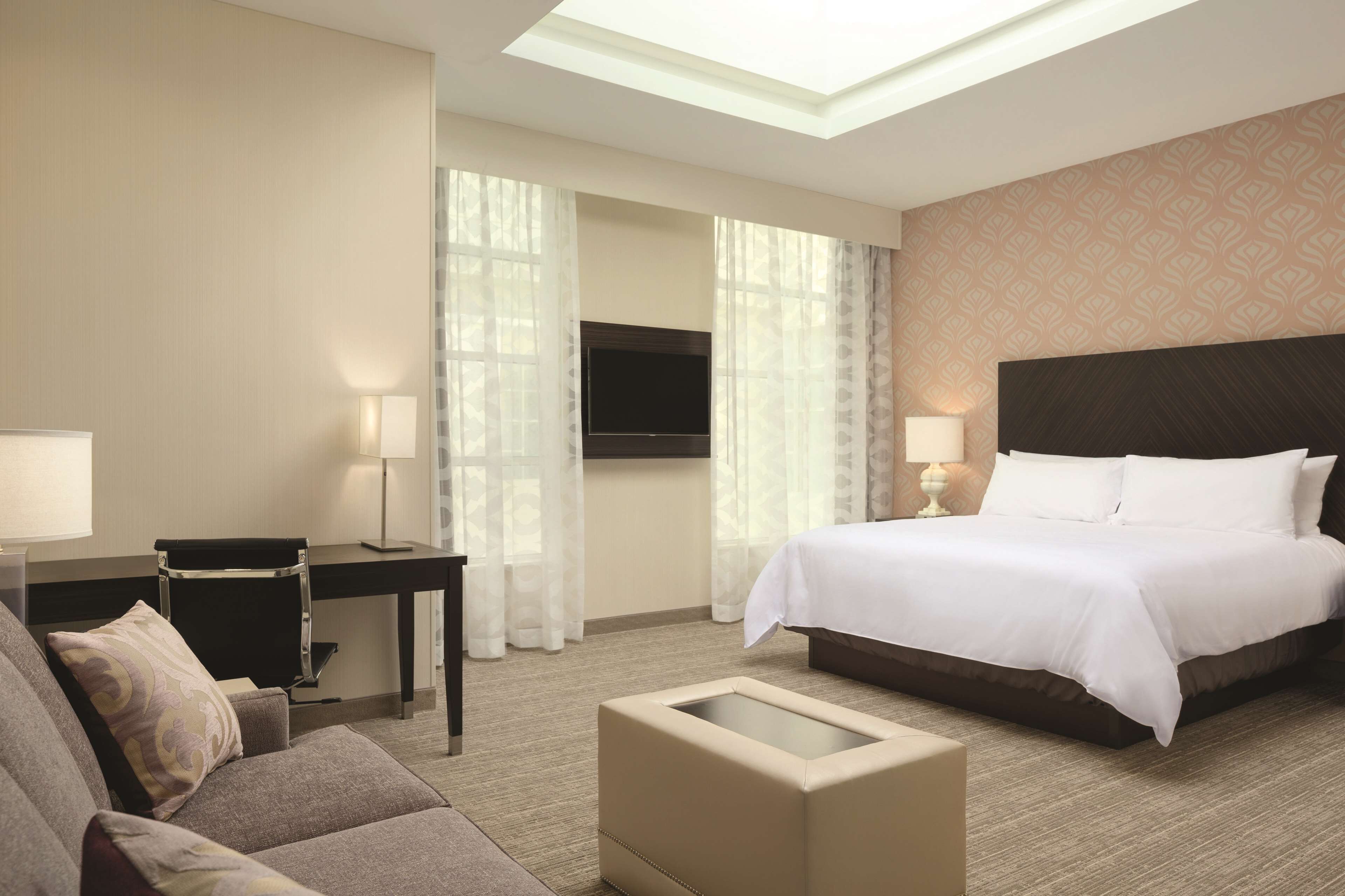 A hotel room with a bed, a desk, a chair, a sofa, and a TV.