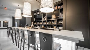 A modern bar area with a long counter, multiple chairs, and a bookshelf filled with bottles.