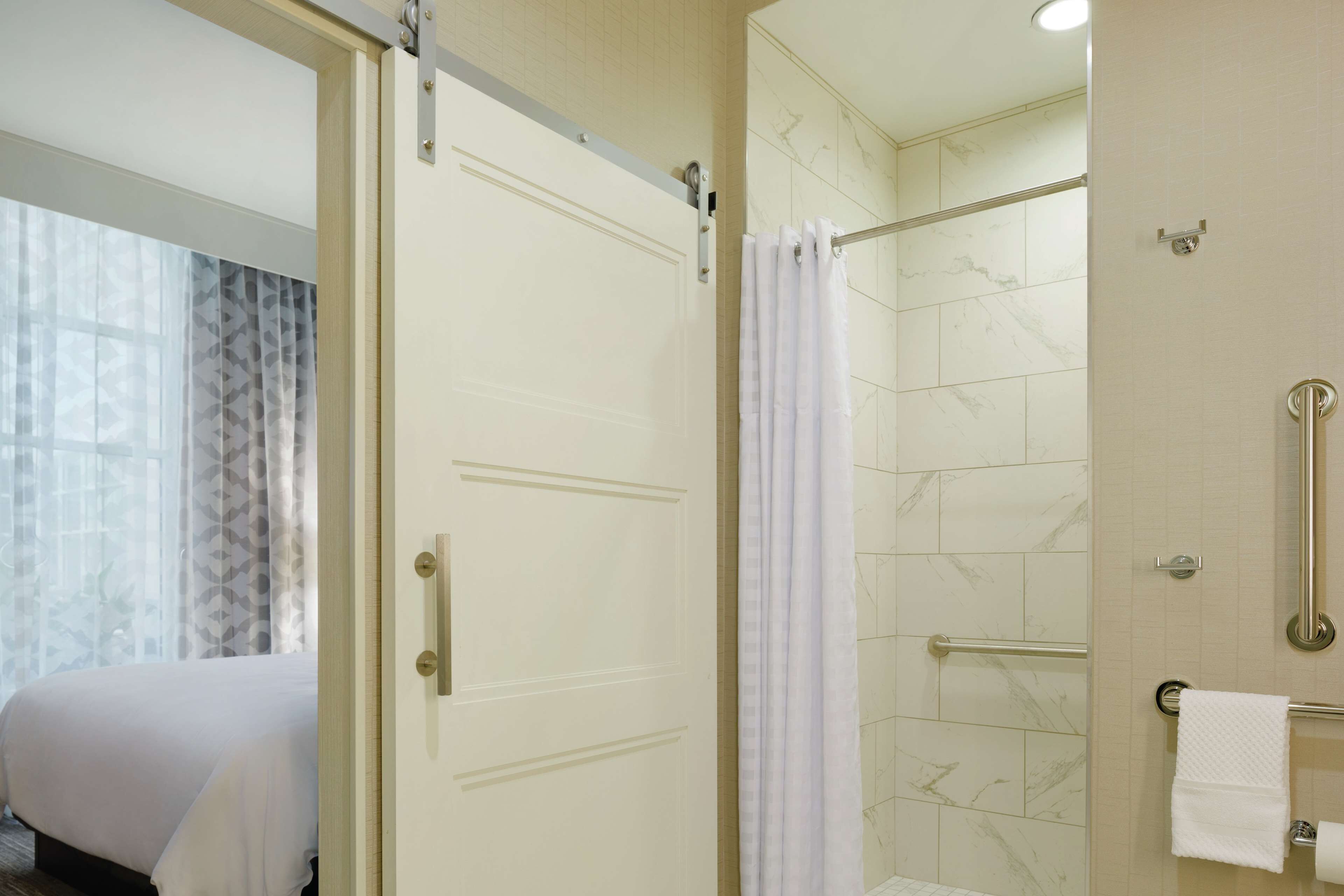 A hotel bathroom with a shower, a toilet with grab bars, and a towel rack.