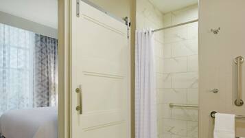 A hotel bathroom with a shower, a toilet with grab bars, and a towel rack.