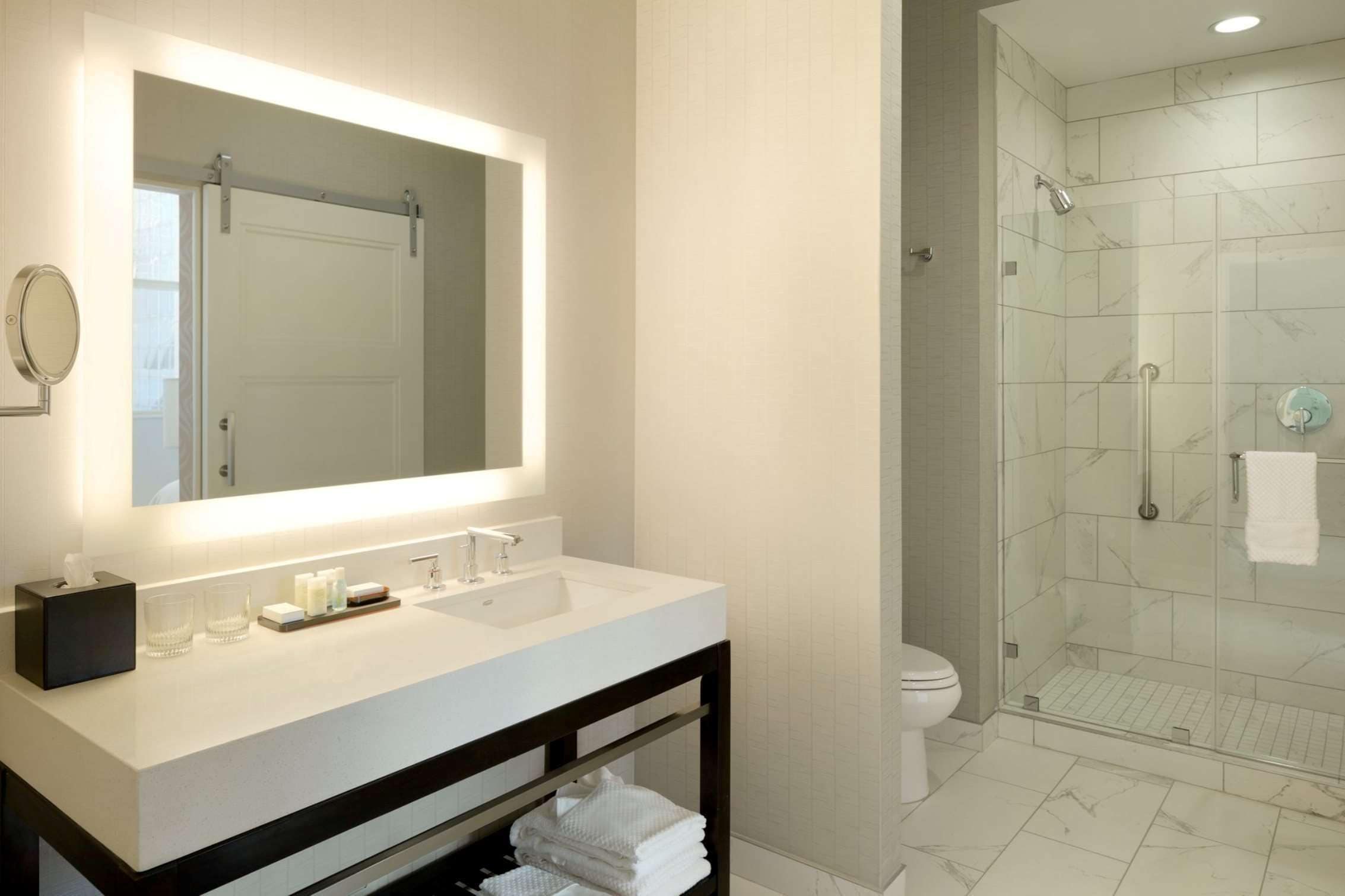 A modern bathroom with a large mirror, white sink, and a glass-enclosed shower.