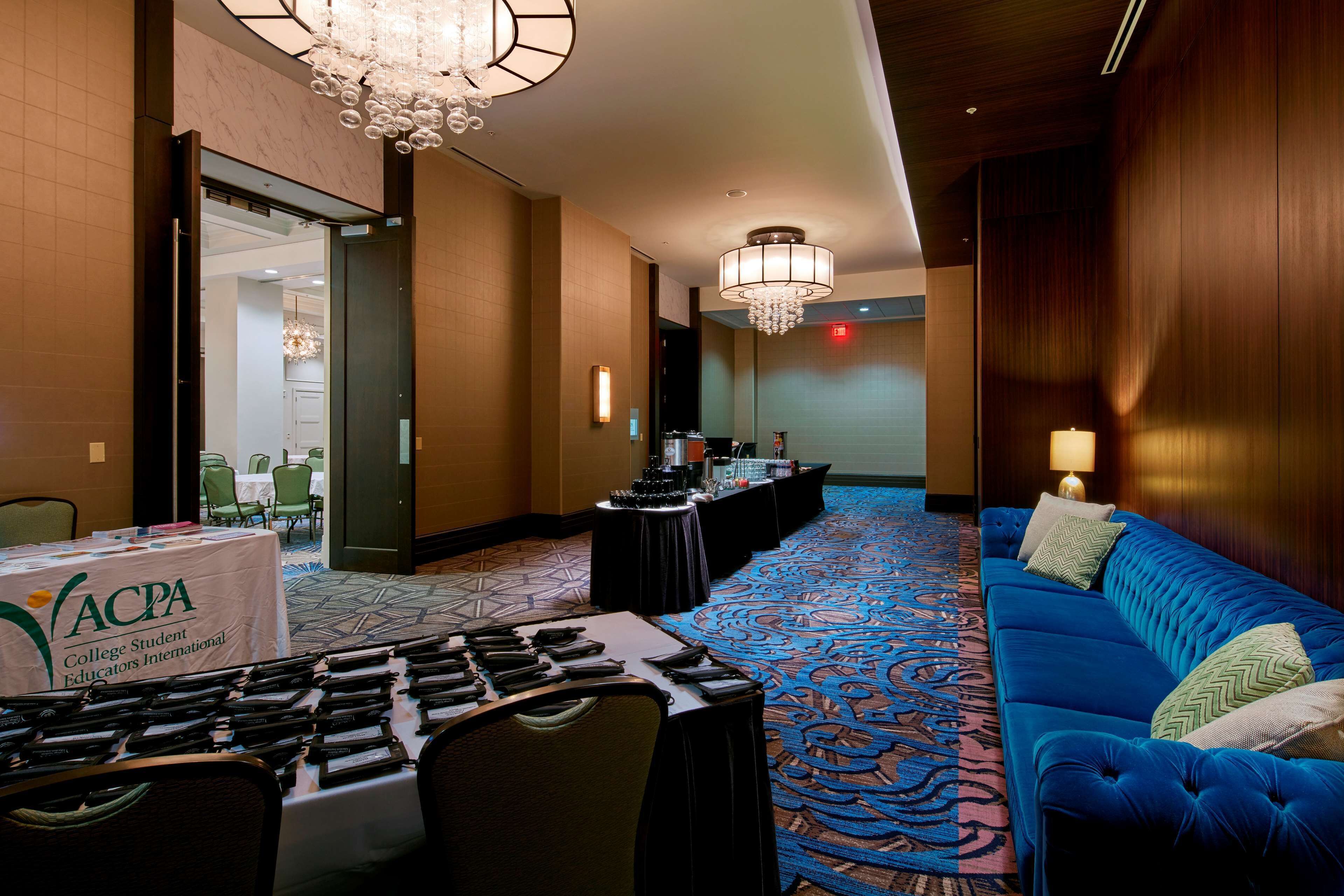 A hotel lobby with a blue sofa, a chandelier, a conference table with laptops, and a carpeted floor.