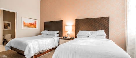 A hotel room with two beds, a nightstand with a lamp, and a framed picture on the wall.