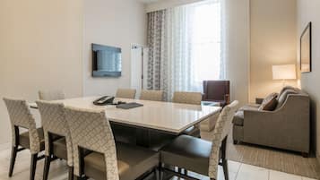 Una habitación de hotel moderna con una mesa de comedor, sillas, un sofá, un televisor y una ventana con cortinas.