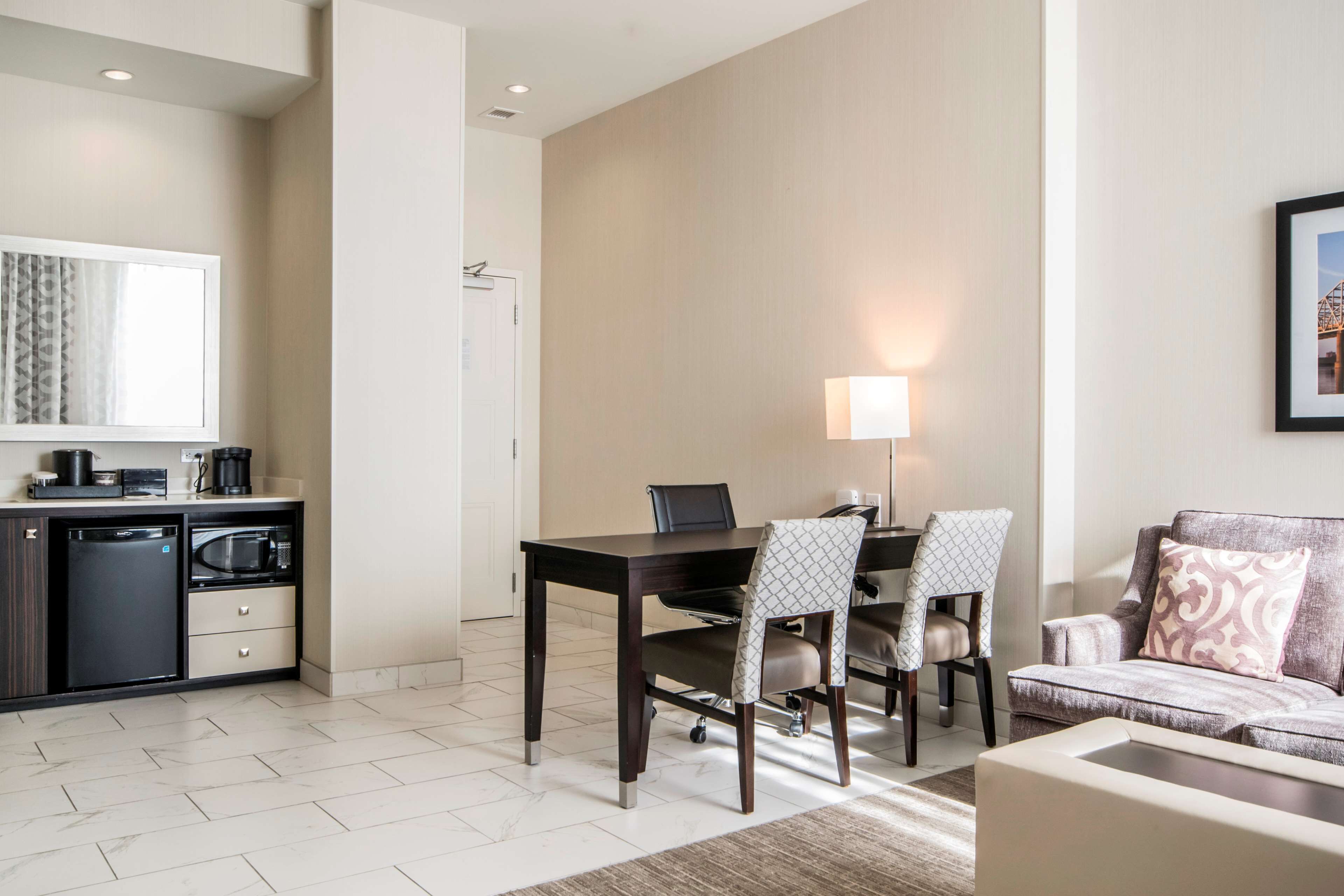 A modern hotel room with a dining area, kitchenette, and seating space.