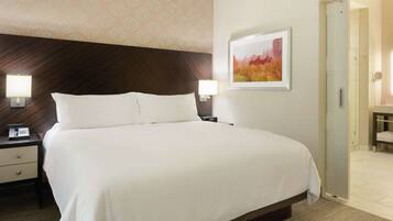 A hotel room with a large bed, bedside lamps, a nightstand, a framed picture on the wall, and a bathroom visible through an open door.
