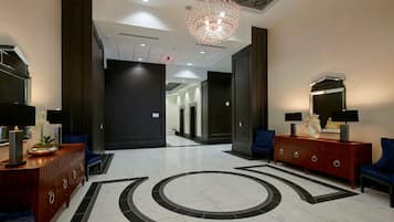 Un hall d’hôtel au design moderne, agrémenté d’un grand lustre, de meubles en bois foncé et clair, et d’un motif décoratif sur le sol.