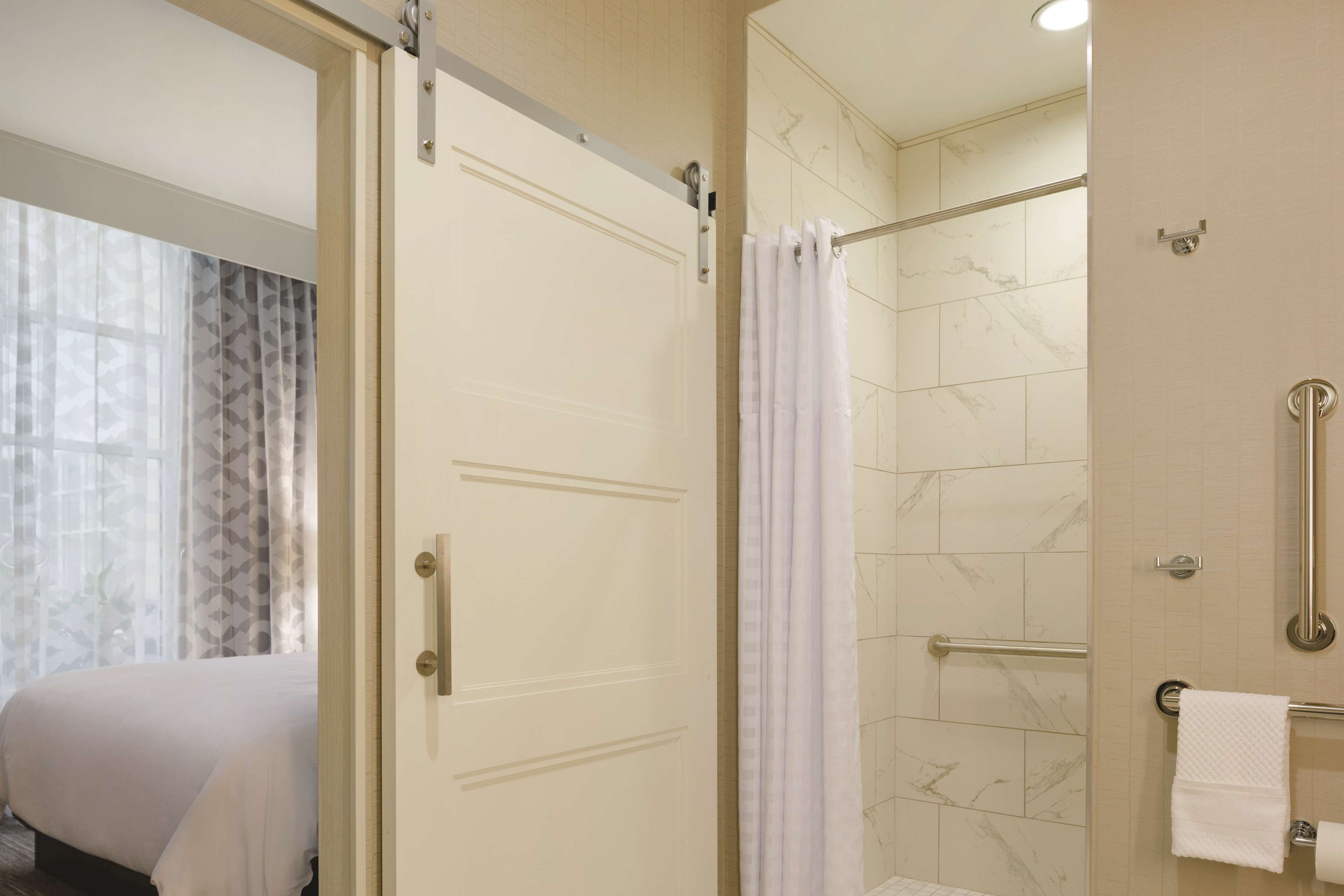 Un baño de hotel con ducha, inodoro con barras de apoyo y un perchero para toallas.
