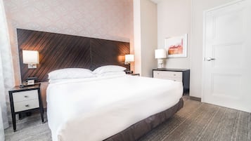 A neatly made bed with a dark headboard, two bedside tables with lamps, a white door, and a patterned wall.