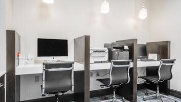 A hotel room with a desk, two chairs, a computer, and a printer.