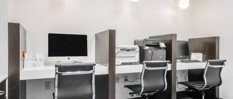 A hotel room with a desk, two chairs, a computer, and a printer.