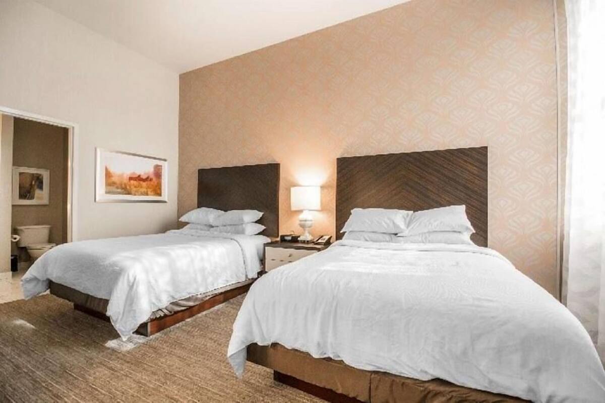 Une chambre d’hôtel avec deux lits, une table de chevet avec une lampe, un tableau au mur et une porte donnant sur une autre pièce.