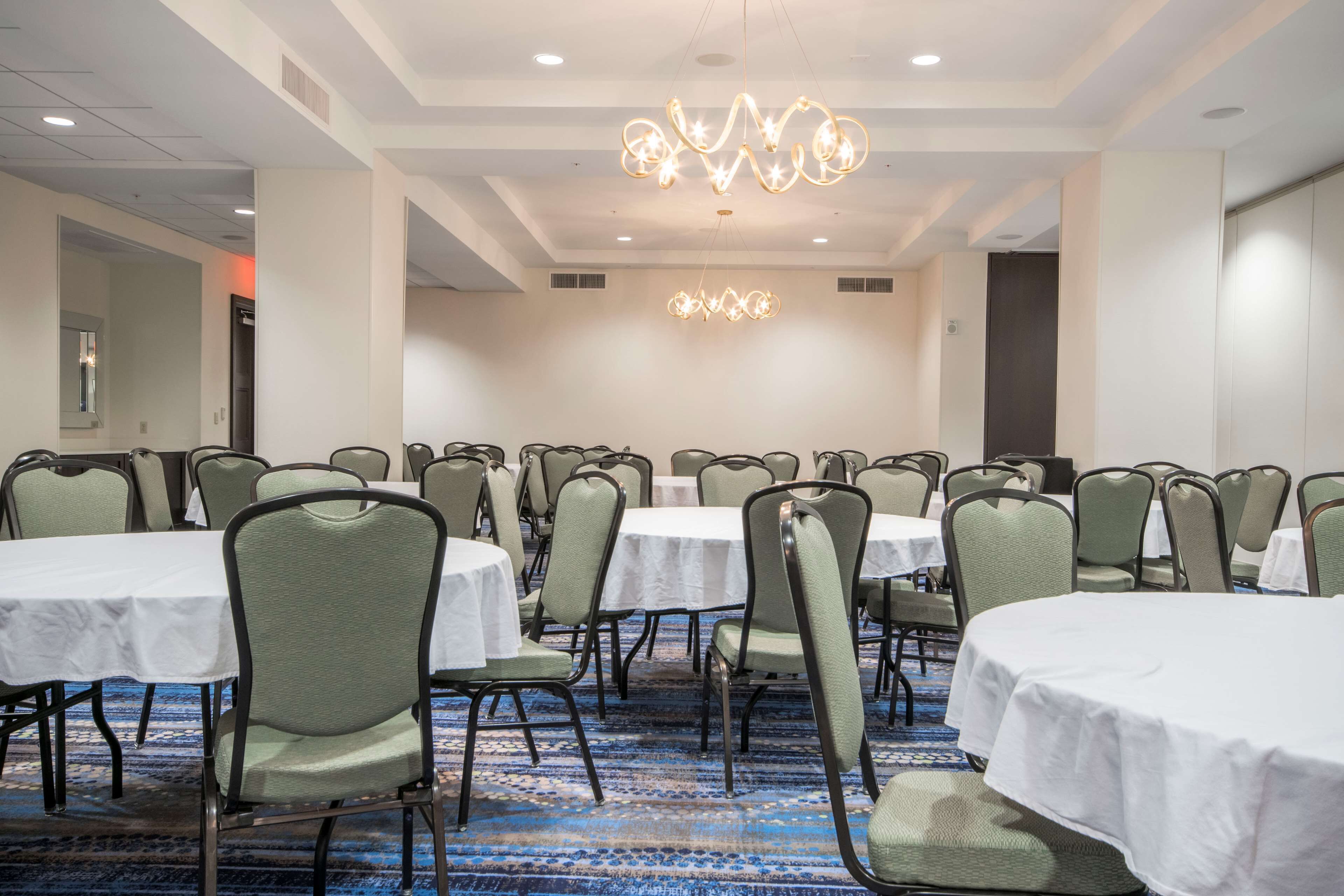 A conference room with round tables and chairs, a chandelier, and a carpeted floor.