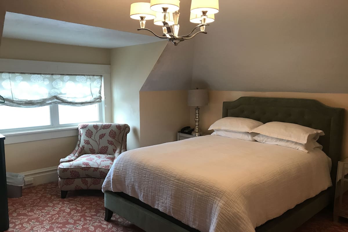 A bedroom with a bed, a chair, a nightstand, and a lamp.