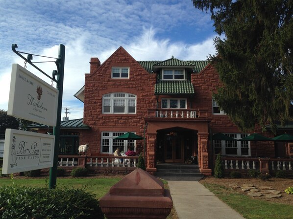 A two-story stone building with a green roof, a balcony, and a sign for 'Thistledown at Nigel House'. - Thistledown At Seger House (Ligonier)