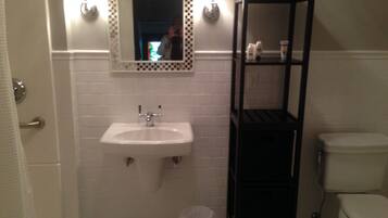 Une salle de bain avec un lavabo blanc, un miroir et une étagère noire.