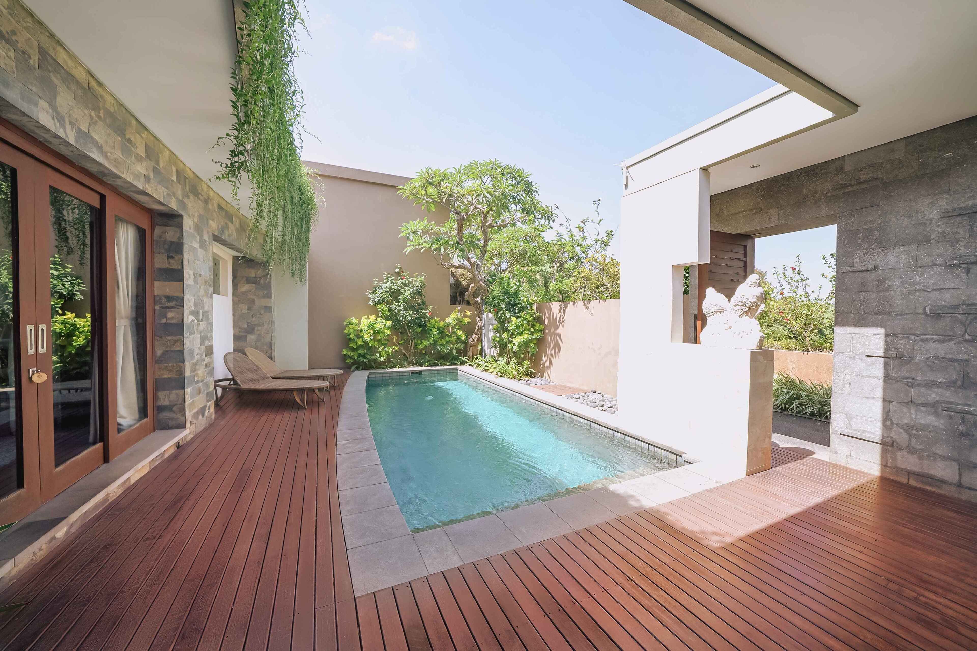 A modern outdoor pool area with a wooden deck, stone walls, and a hanging plant.
