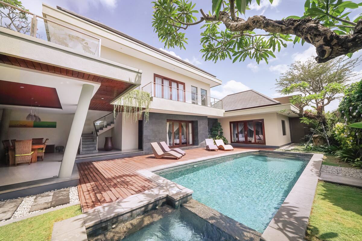 A modern house with a swimming pool, wooden deck, and a staircase leading to a balcony.