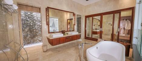 A spacious bathroom with a large bathtub, a double vanity with a stone accent wall, and a large mirror.