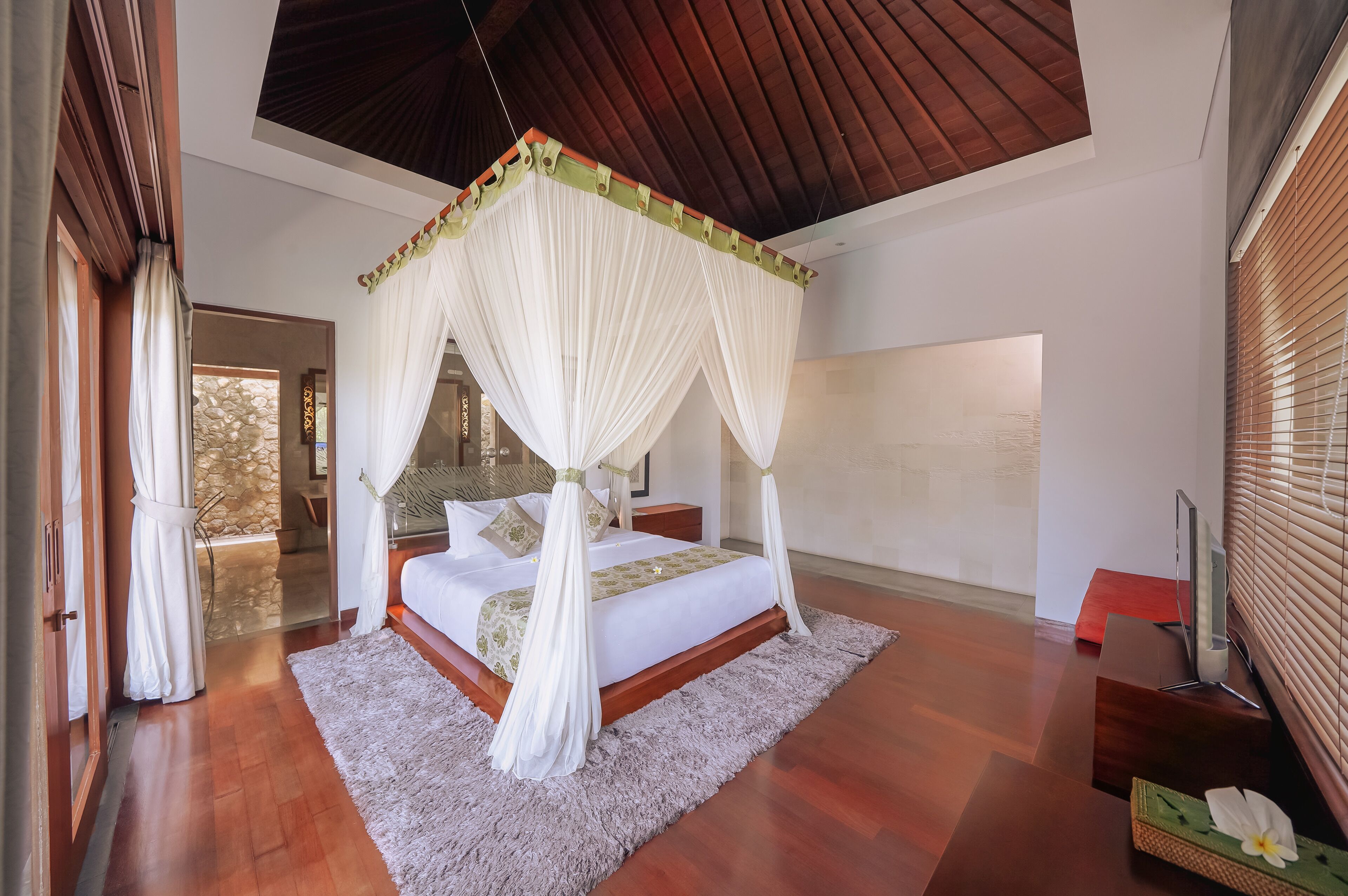 Un dormitorio amplio con cama con dosel, pared de piedra y vistas al exterior.