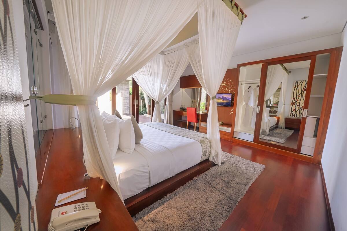 A bedroom with a bed, white curtains, a bedside telephone, and a mirror.