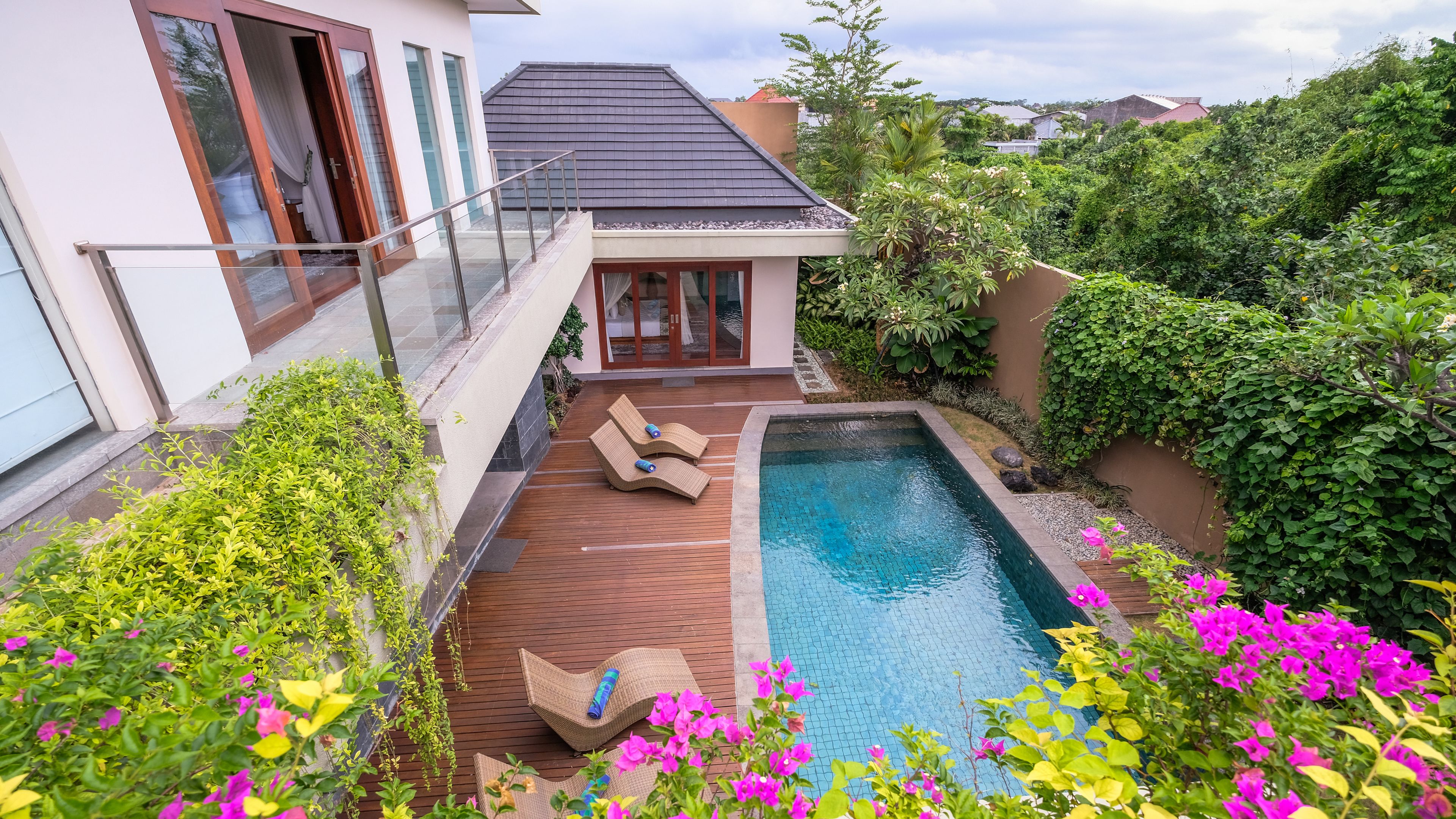 A modern house with a swimming pool, two lounge chairs, and lush greenery.