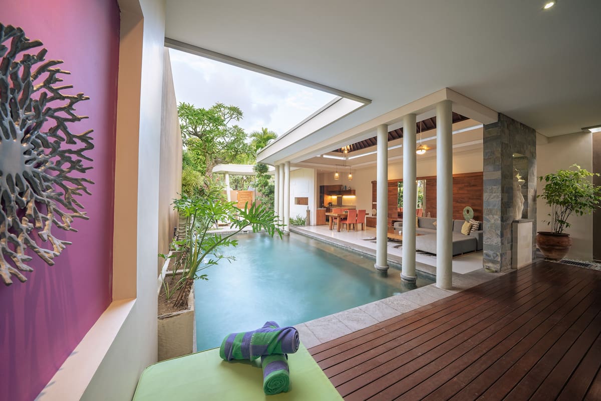 A modern indoor pool area with a wooden deck, a lounge with seating, and a view of the outdoors.
