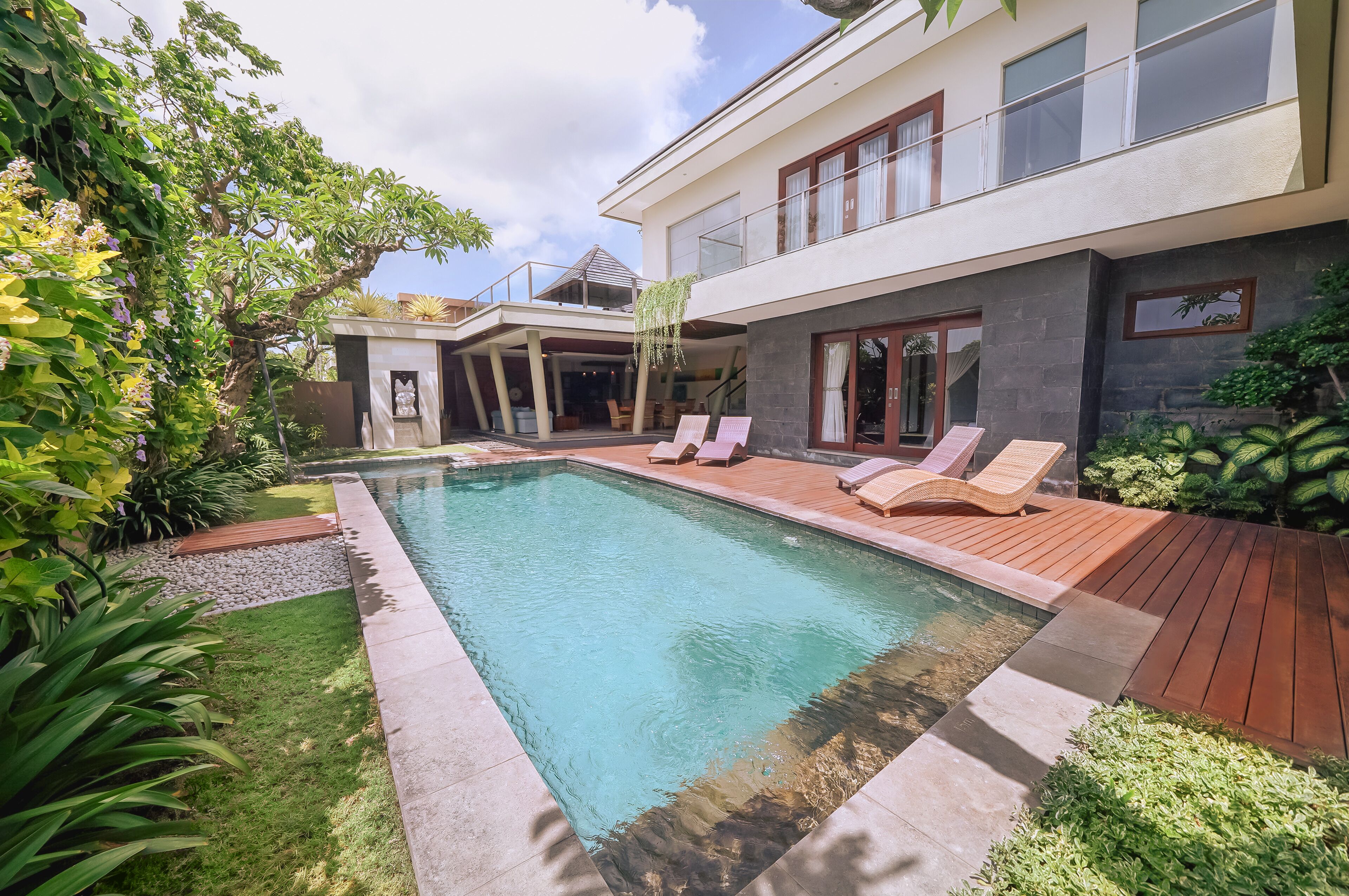 A modern house with a swimming pool, wooden deck, and lush greenery.