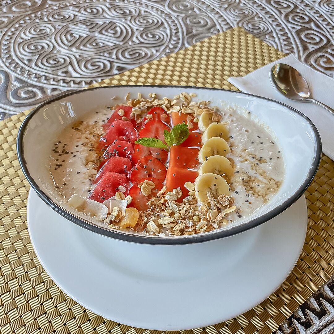 A bowl of oatmeal topped with strawberries, banana slices, and granola on a woven placemat.