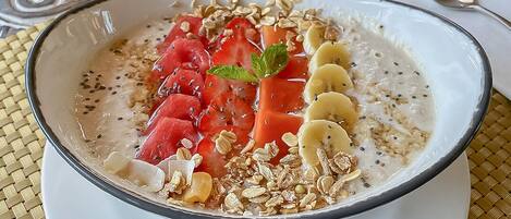 A bowl of oatmeal topped with strawberries, banana slices, and granola on a woven placemat.