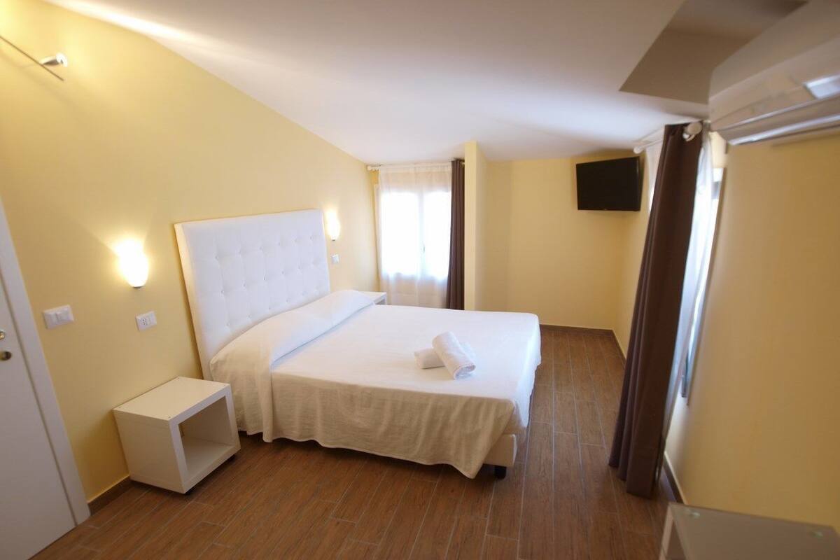 A bedroom with a bed, bedside table, and a flat-screen TV on the wall.