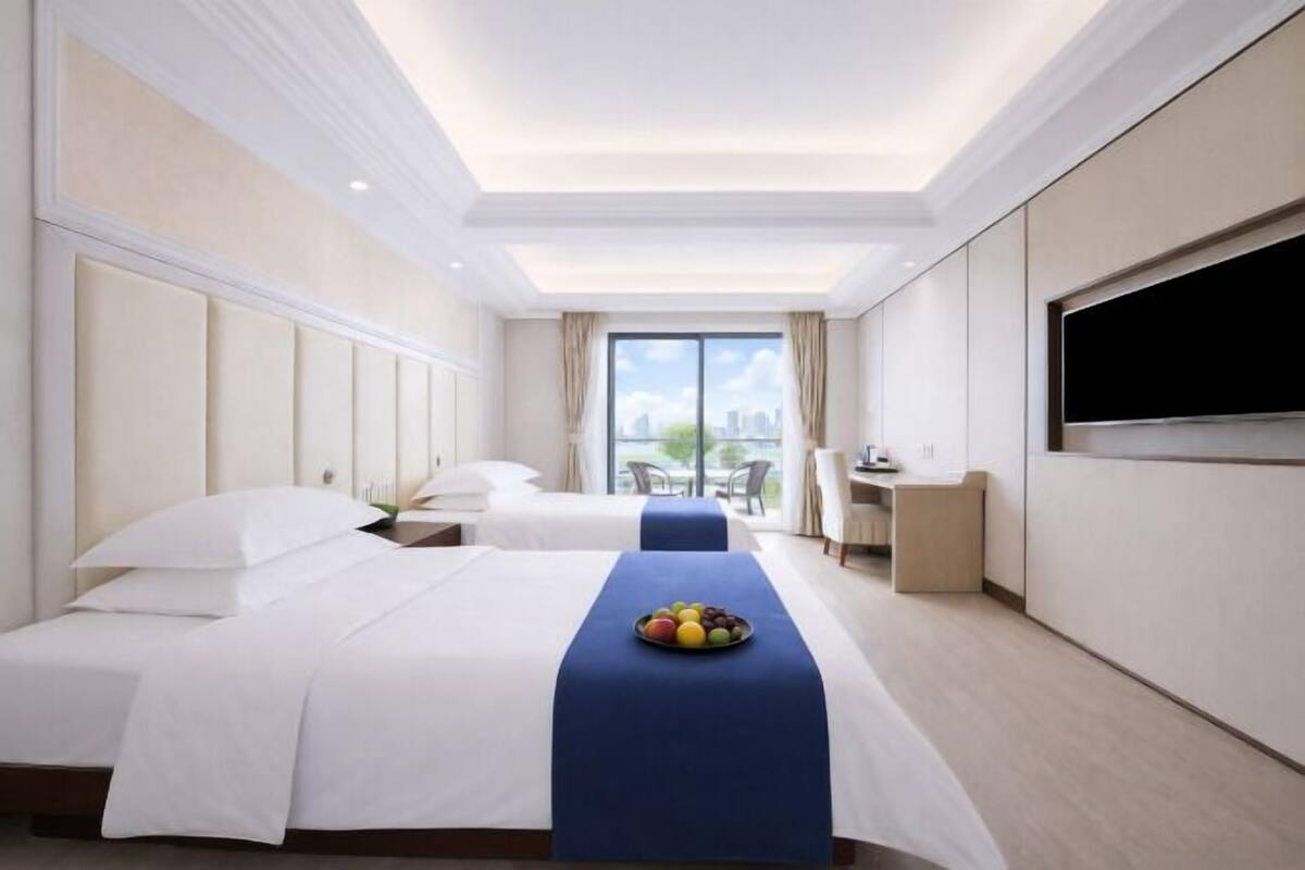 Een hotelkamer met twee bedden, een televisie, een bureau en een balkon met uitzicht over de stad.