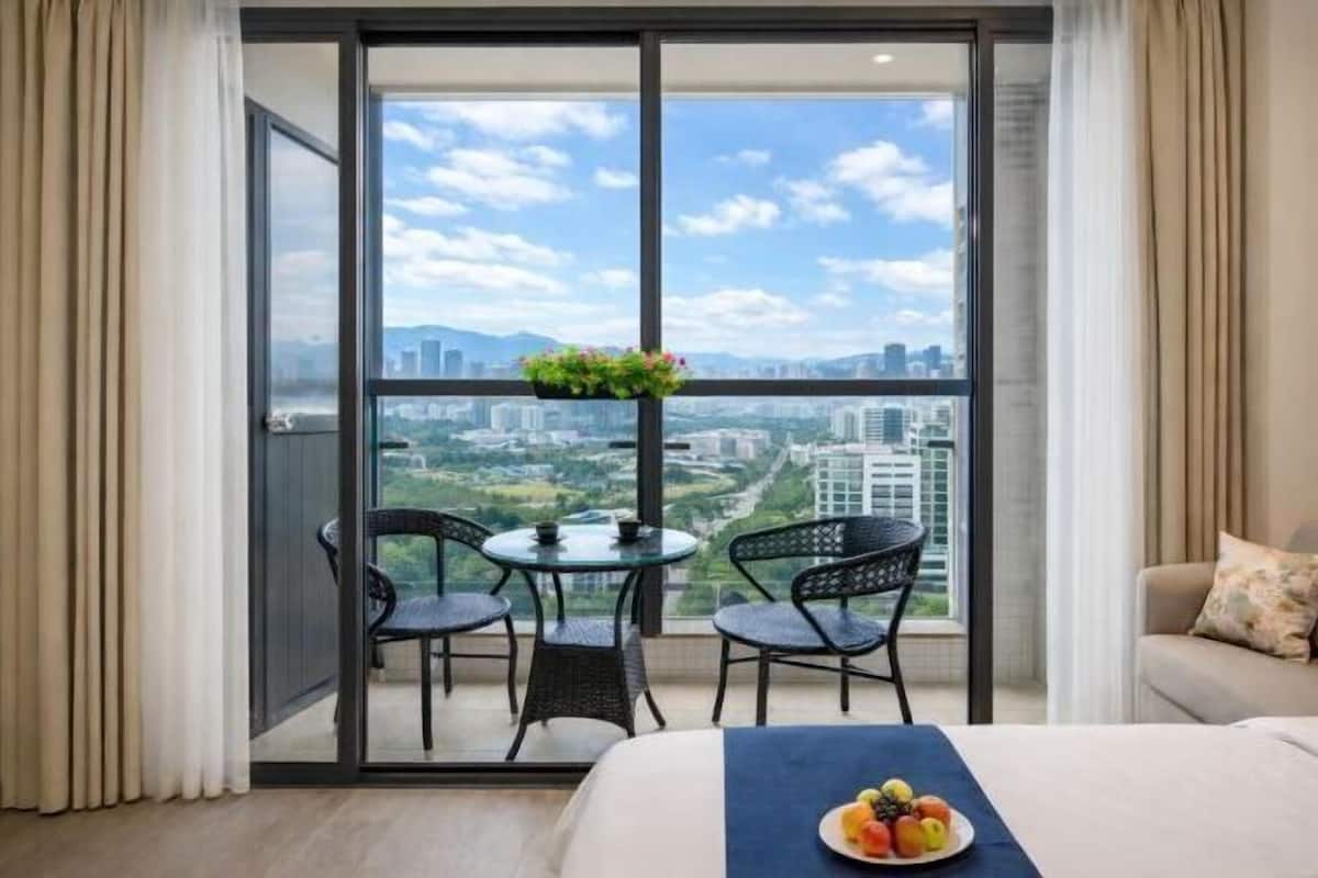 Een balkon met een tafel en stoelen, een bed met een blauwe sprei en een uitzicht op een stadsbeeld.