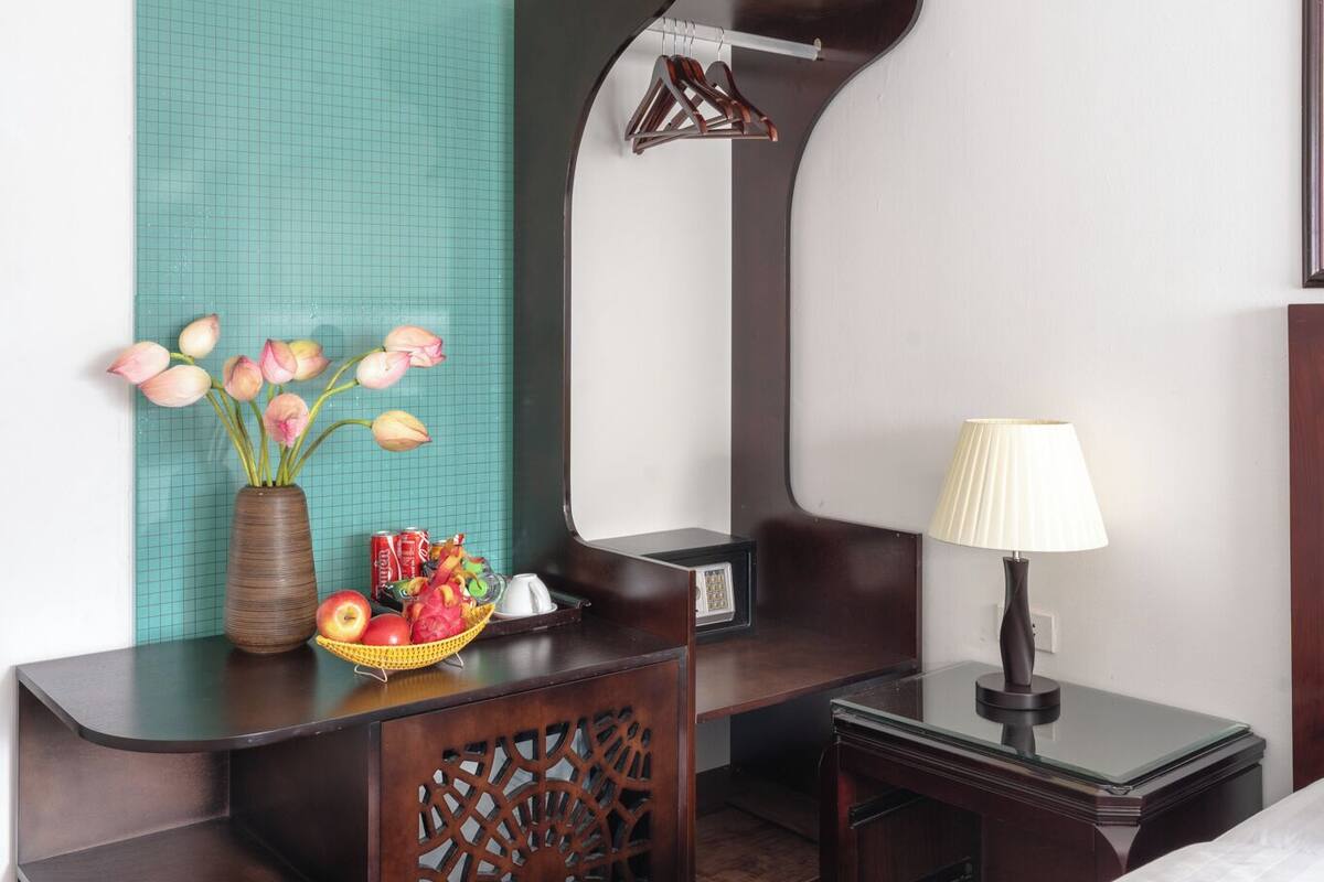 A hotel room with a wooden desk, a vase of flowers, a lamp, and a bed.