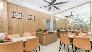 A modern dining area with wooden panel walls, a central counter with a fruit display, and a view of a garden through large windows. - Little Hanoi Hotel (Hanoi)