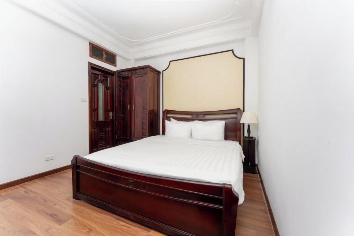 A bedroom with a wooden bed, a wardrobe, and a nightstand with a lamp.