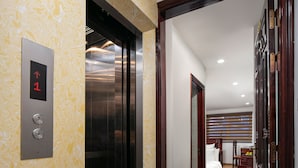 A hotel hallway with an elevator, a bed, and a wooden door. - Little Hanoi Hotel (Hanoi)